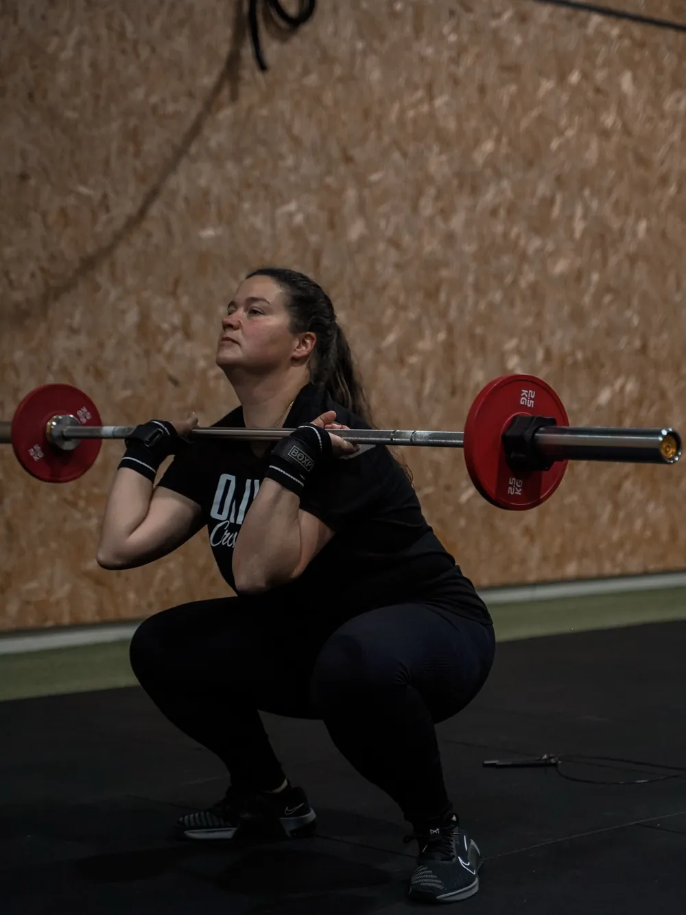 Atleta a fazer agachamento com barra junto à parede de madeira