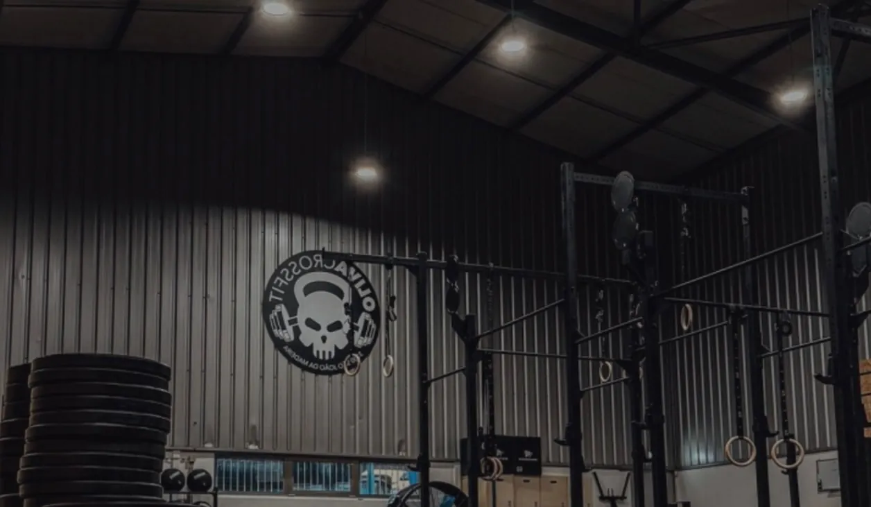 Interior da box com racks, argolas e o logótipo da Oliva CrossFit na parede